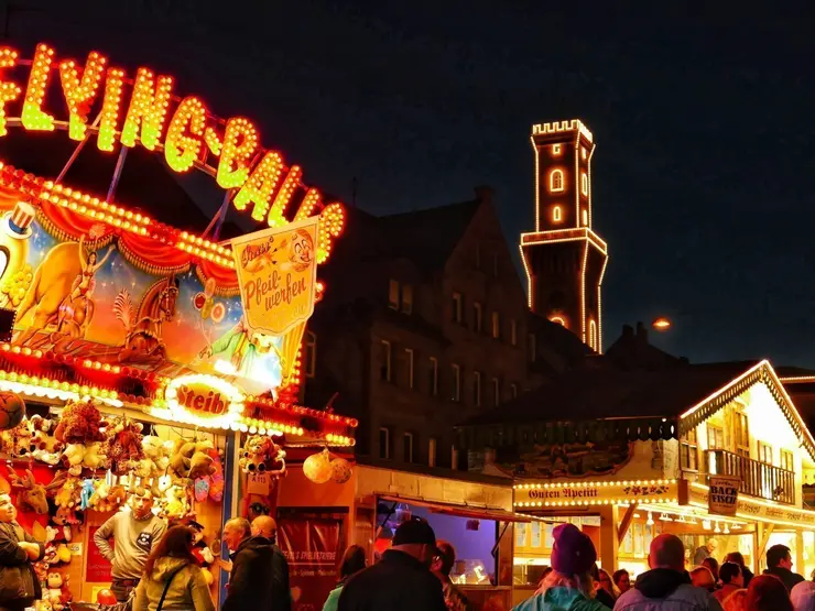 Das Kirchweihgelände mit Buden am Abend und dem beleuchteten Rathausturm im Hintergrund